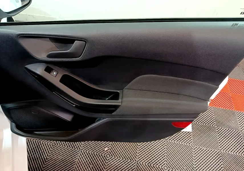 Vue rapprochée de la porte avant gauche noire d’une Ford Fiesta blanche, avec poignée et commande de vitre visible.