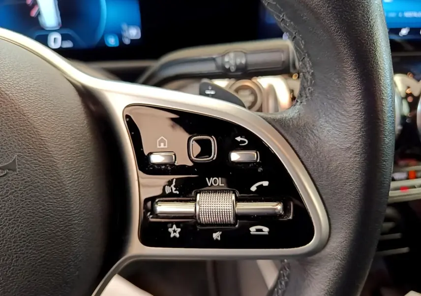 Gros plan sur la commande de volume et boutons multifonctions sur le côté gauche du volant cuir noir du Mercedes GLB 200 d gris foncé.
