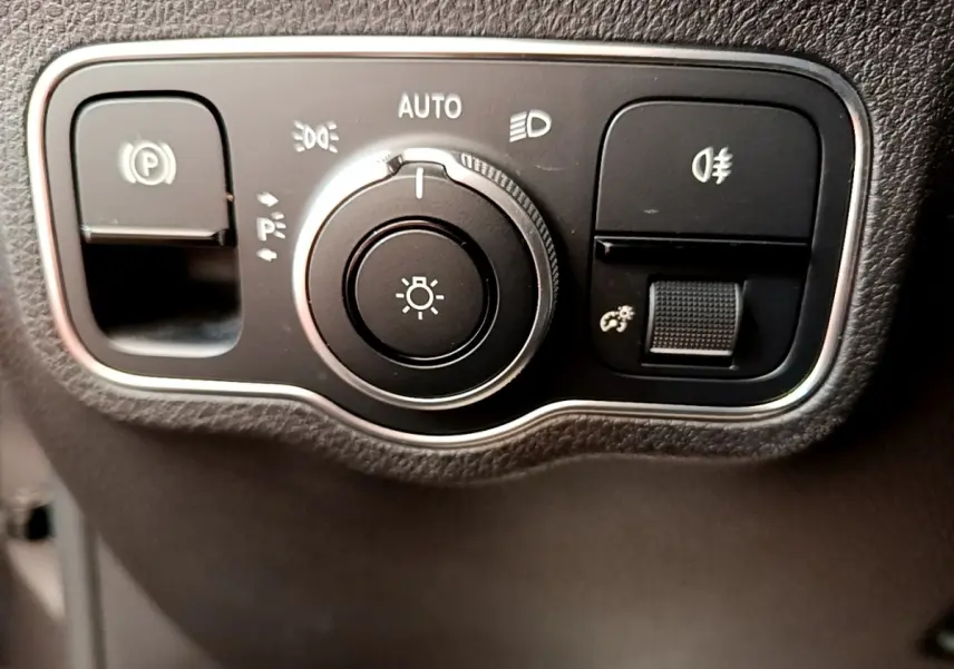 Gros plan sur le bouton de commande des phares et du frein à main électrique dans l'habitacle noir du Mercedes GLB 200 d.