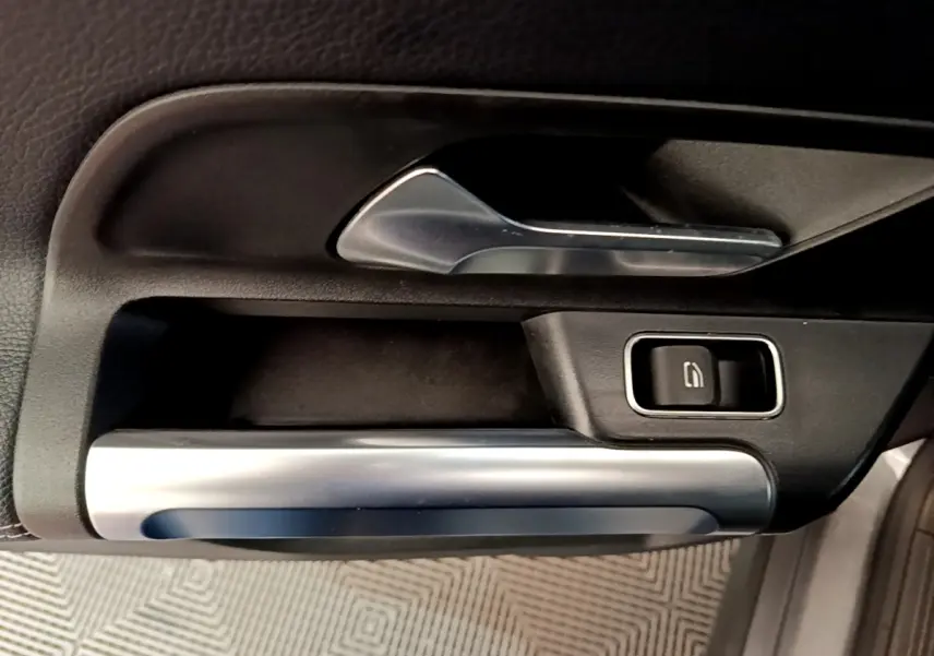 Gros plan sur la poignée intérieure et commande de vitre de la porte avant droite du Mercedes GLB 200 d gris foncé.