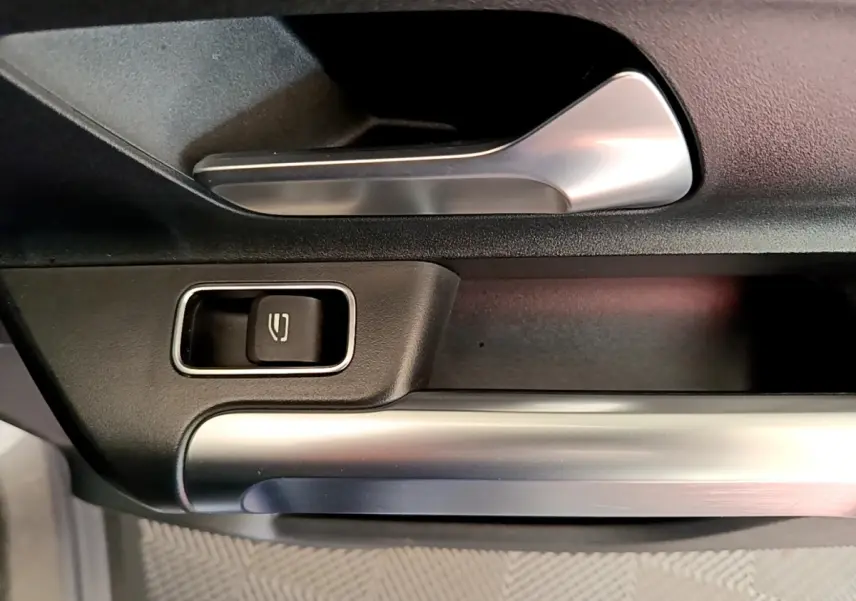 Détail de la poignée intérieure et bouton de lève-vitre sur la porte côté conducteur d’un Mercedes GLB gris foncé.