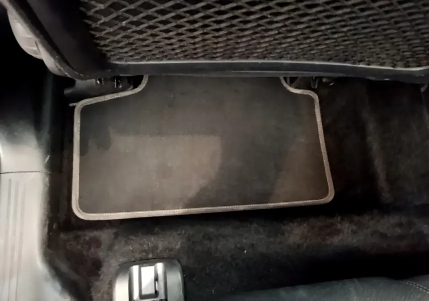 Vue rapprochée du tapis de sol gris foncé au sol, avec filet de rangement sous le siège arrière d’un Mercedes GLB 200 d.