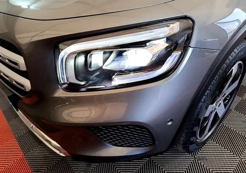 Gros plan sur le phare avant droit et la calandre d’un Mercedes GLB 200 d Business Line gris foncé.