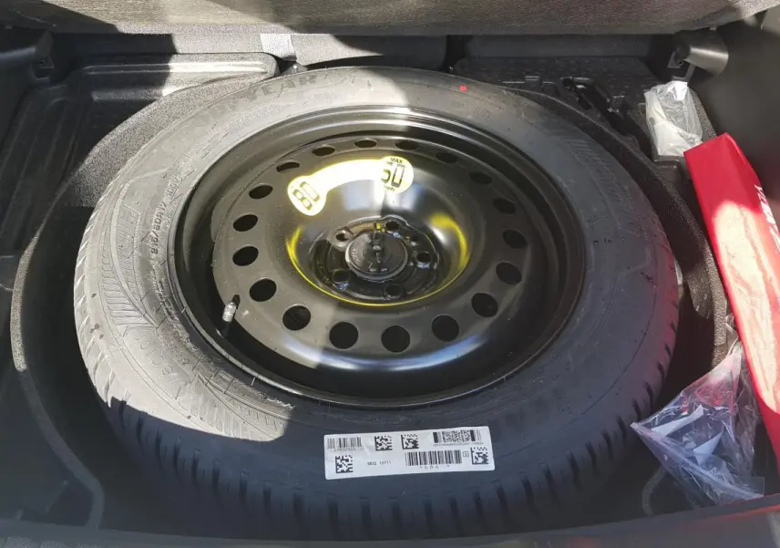 Roue de secours noire en acier dans le coffre du Jeep Compass blanc 2024, avec kit de réparation visible à droite.