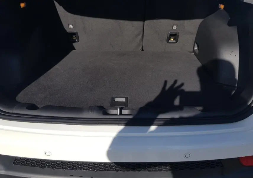 Coffre ouvert vu de l'arrière d'un Jeep Compass blanc 2024 avec tapis de sol noir et feux arrière visibles.