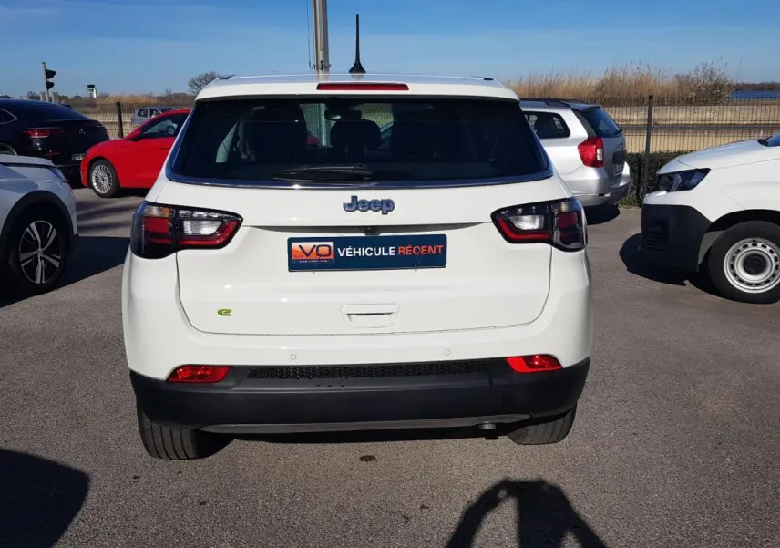 Vue arrière d'un Jeep Compass blanc 2024 avec feux LED et badge e-Hybrid sur un parking extérieur.
