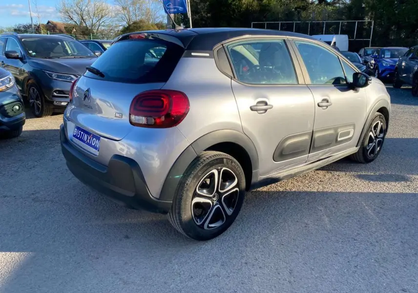Vue 3/4 arrière droite d'une Citroën C3 gris Artense avec toit noir et protections latérales caractéristiques.