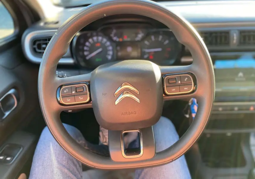 Vue centrée sur le volant de la Citroën C3 2022, avec commandes intégrées et tableau de bord flou en arrière-plan.