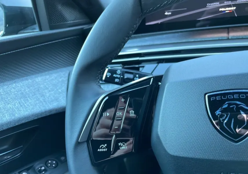Gros plan sur le volant cuir du Peugeot 5008 gris titane 2025, avec commandes intégrées et logo lion central.