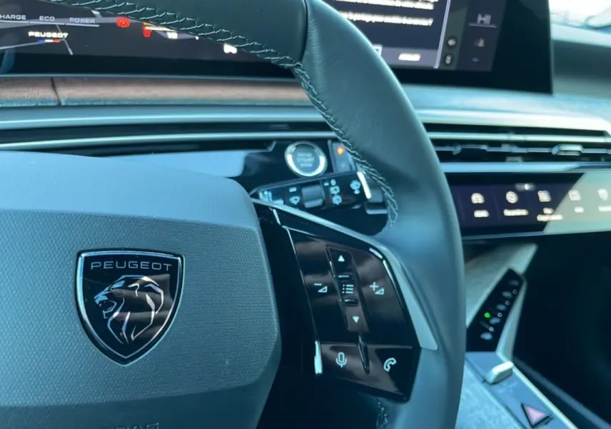 Gros plan sur le volant cuir noir du Peugeot 5008 Hybrid 145 Allure Plus 2025 avec commandes intégrées et tableau de bord digital.