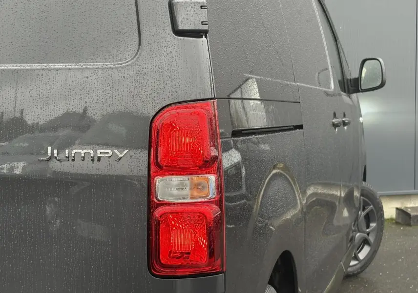 Vue arrière côté droit du Citroën Jumpy gris titane avec feux arrière rouges et portes tôlées sous la pluie.
