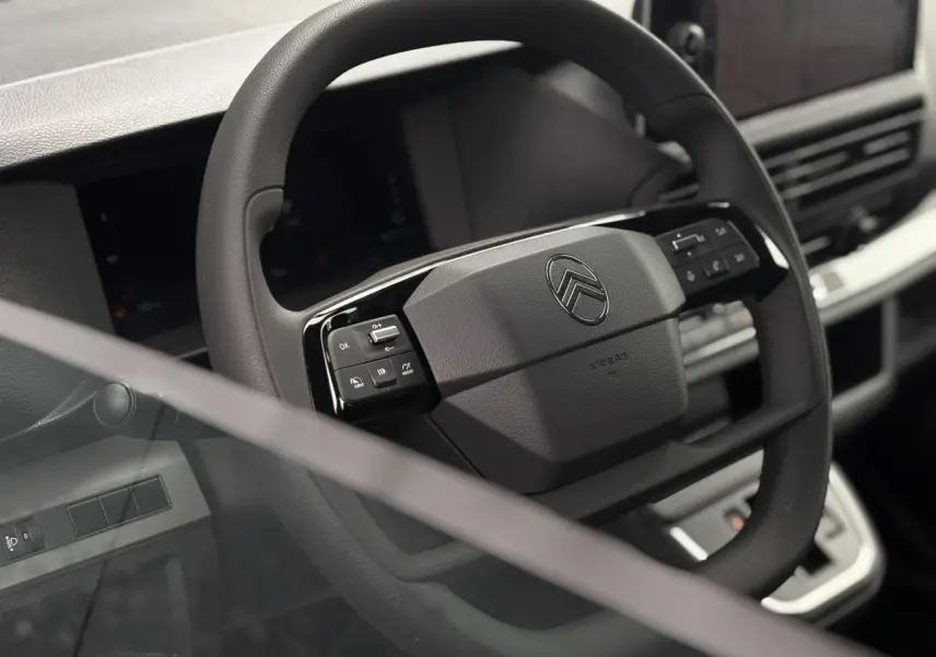 Gros plan sur le volant noir du Citroën Jumpy 2025, avec commandes intégrées et tableau de bord numérique en arrière-plan.