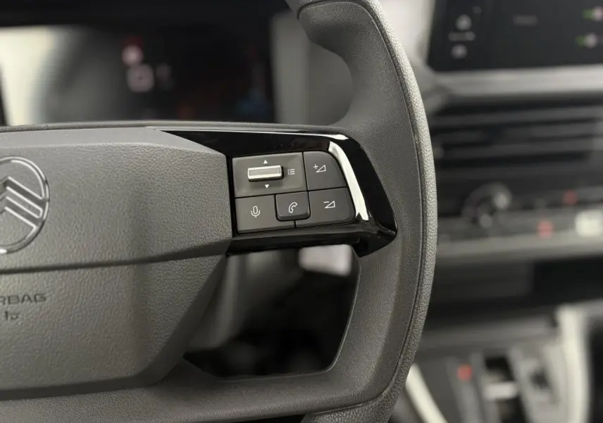 Gros plan sur les commandes audio et vocales du volant du Citroën Jumpy 2025, intérieur gris et noir flouté en arrière-plan