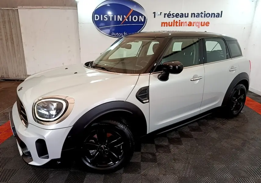Vue 3/4 avant droit d'une MINI Countryman gris clair avec toit noir et jantes noires dans un showroom.