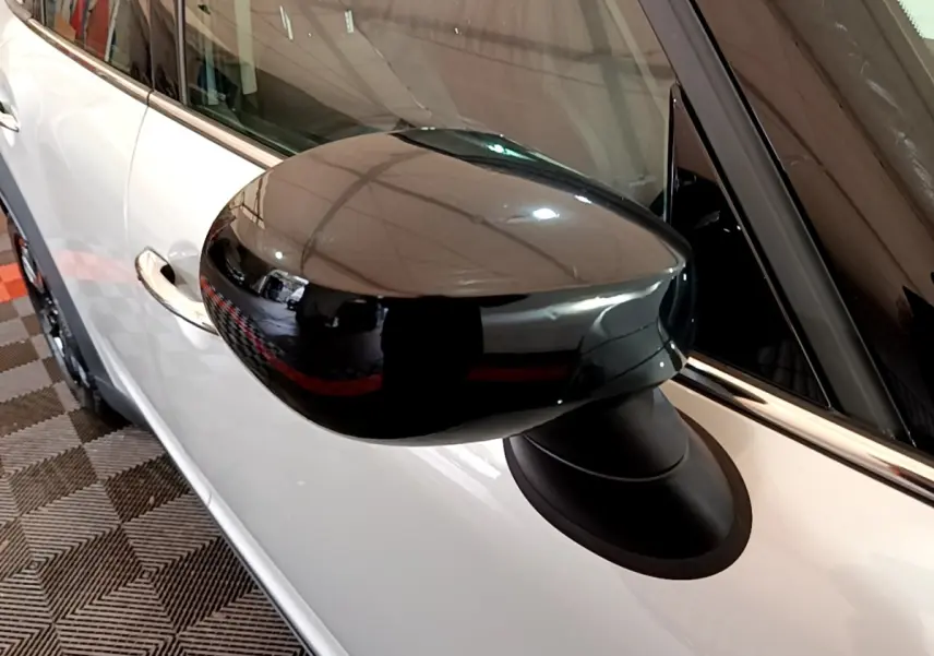 Gros plan sur le rétroviseur noir brillant côté gauche d'une MINI Countryman gris clair, avec poignée de porte visible.