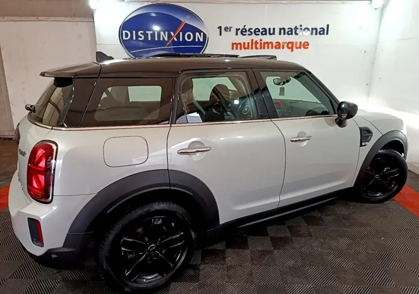 Vue côté droit arrière d'une MINI Countryman gris clair avec toit noir et jantes noires brillantes en intérieur showroom.