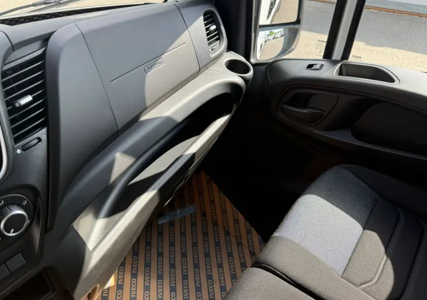 Vue intérieure côté passager du tableau de bord et siège tissu gris foncé de l'IVECO Daily blanc 2026.