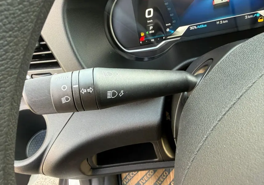 Gros plan sur la commande des phares et clignotants à gauche du volant dans l’habitacle du fourgon Iveco Daily blanc.