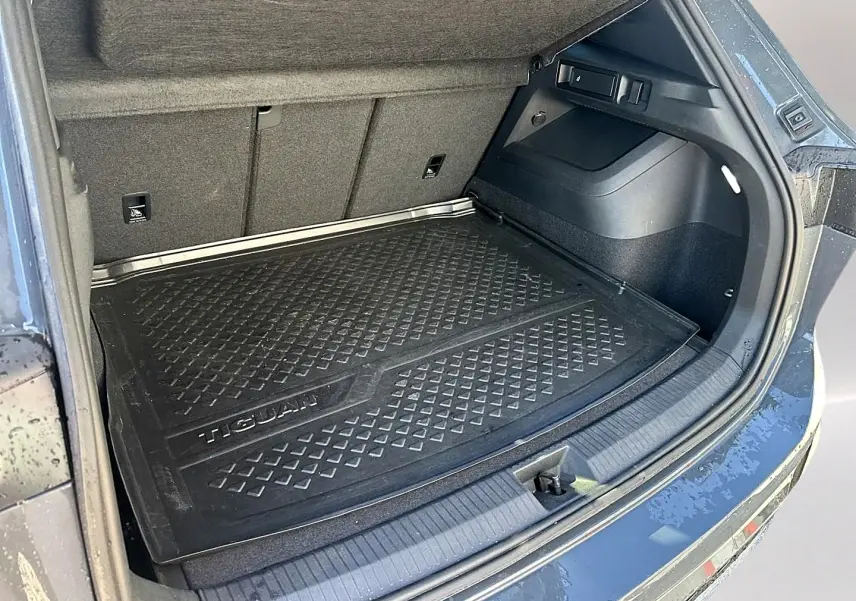 Coffre ouvert vu de l'arrière droit d'un Volkswagen Tiguan gris dauphin avec tapis de protection noir marqué Tiguan.
