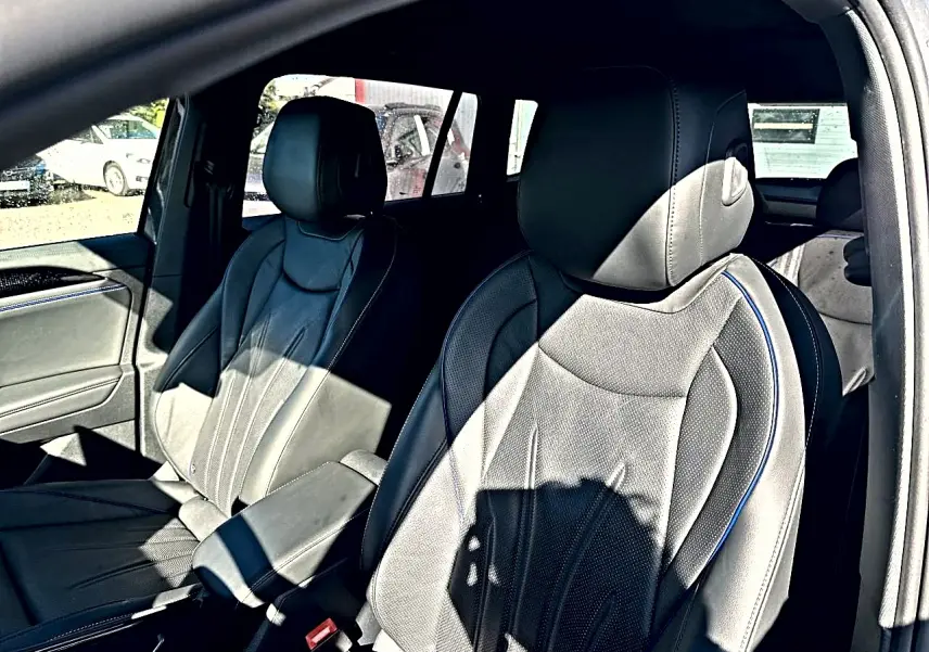 Vue intérieure côté avant droit du Volkswagen Tiguan 2024 gris dauphin, sièges cuir noir avec surpiqûres bleues et accoudoir central.