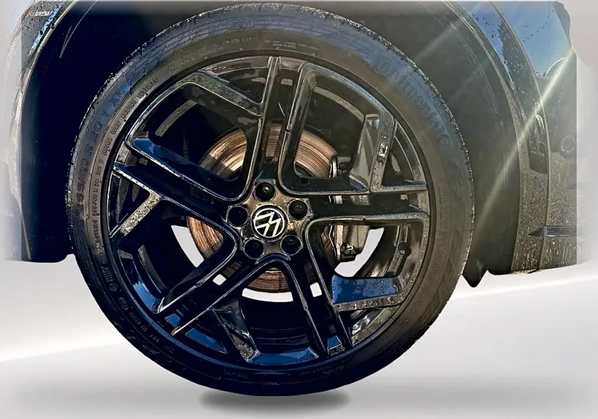 Gros plan sur la jante alu noire brillante du Volkswagen Tiguan gris dauphin, mettant en valeur le logo VW central.