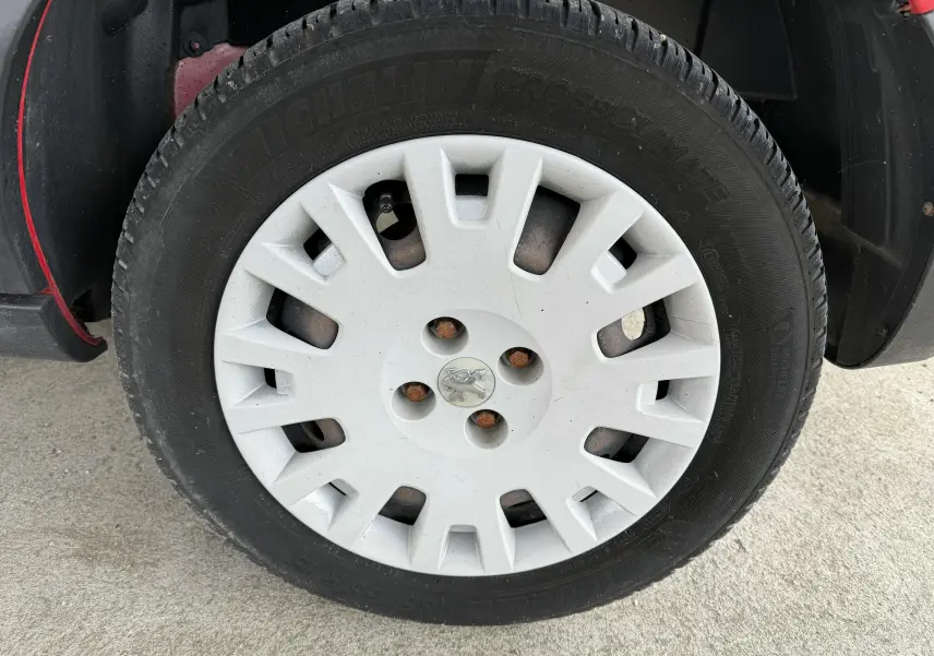 Gros plan sur la roue avant gauche d’un Peugeot Bipper Tepee rouge avec enjoliveur blanc et logo Peugeot central.