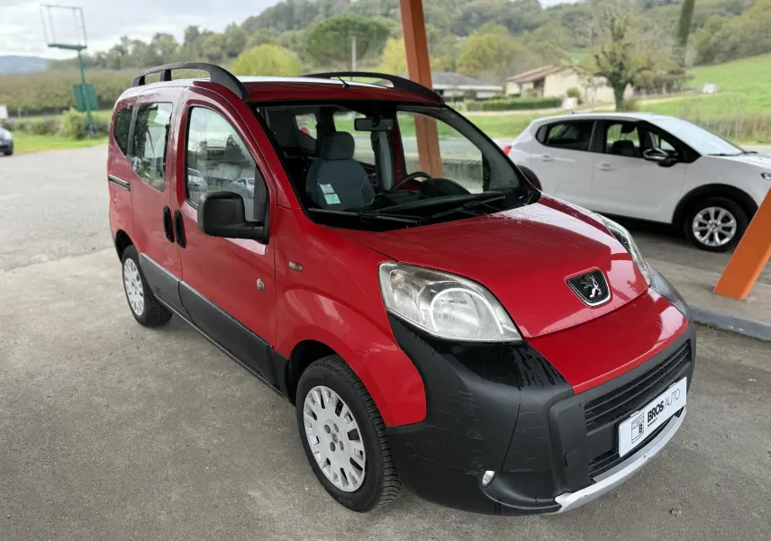Vue 3/4 avant d'un Peugeot Bipper Tepee rouge avec pare-chocs noir et jantes 15 pouces sous abri extérieur.