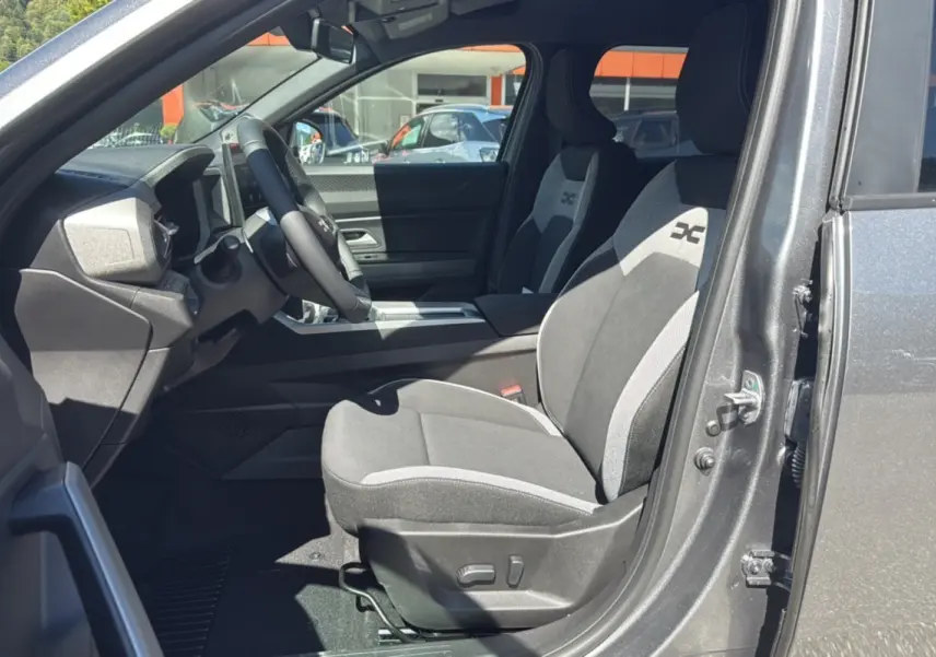 Intérieur côté conducteur du Dacia Bigster gris schiste 2025, sièges tissu avec logo X et volant cuir.