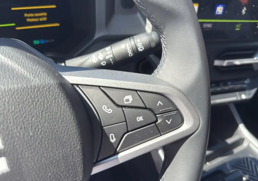 Gros plan sur les commandes au volant cuir du Dacia Bigster Hybrid 155 gris schiste, avec tableau de bord digital en arrière-plan.