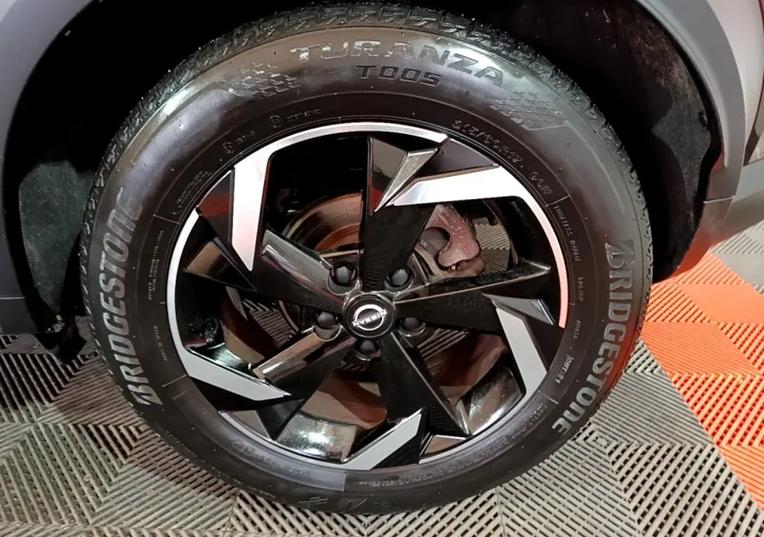 Gros plan sur la roue avant gauche du Nissan Juke Hybrid 143 Business+ noir avec jante alliage bicolore et pneu Bridgestone.