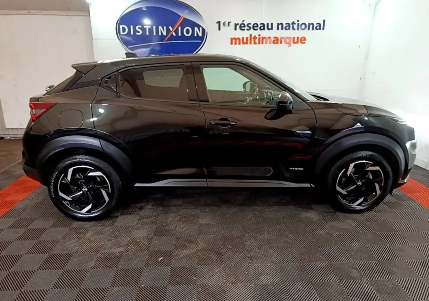 Profil droit d'un Nissan Juke Hybrid 143 Business+ noir, avec jantes noires et logo Hybrid visible sur la porte avant.