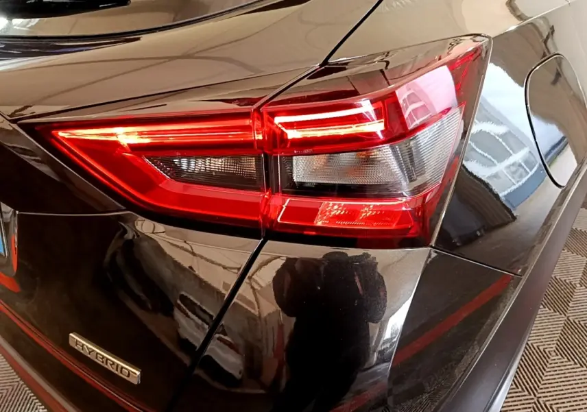 Gros plan sur le feu arrière droit rouge et blanc d’un Nissan Juke Hybrid noir brillant avec badge Hybrid visible.