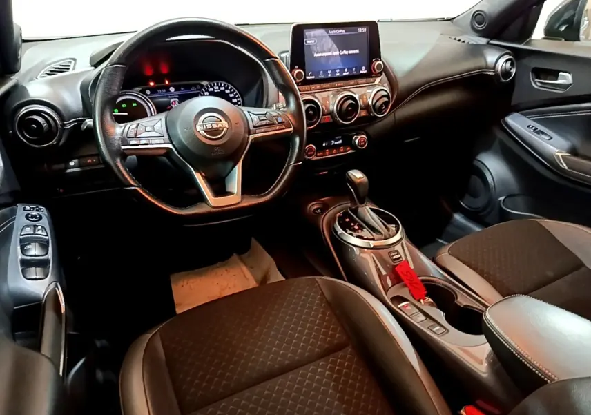 Intérieur noir du Nissan Juke Hybrid 2022 vu côté conducteur, avec volant multifonctions et écran tactile central.