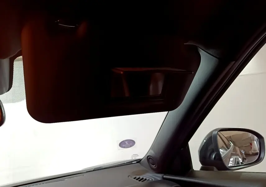 Vue intérieure côté conducteur du Nissan Juke Hybrid 143 Business+ noir, avec pare-soleil et rétroviseur extérieur visible.