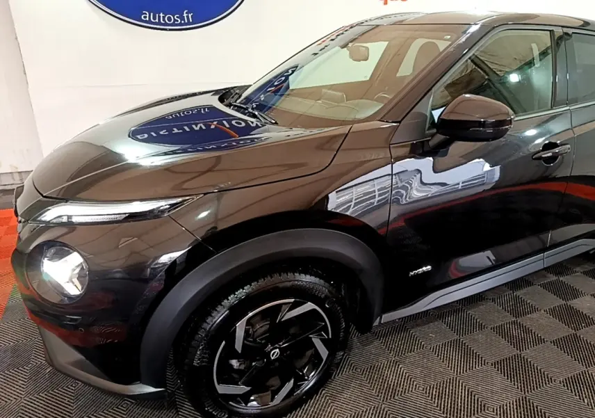 Vue 3/4 avant droit du Nissan Juke Hybrid 143 Business+ noir brillant avec jantes noires et phares allumés.