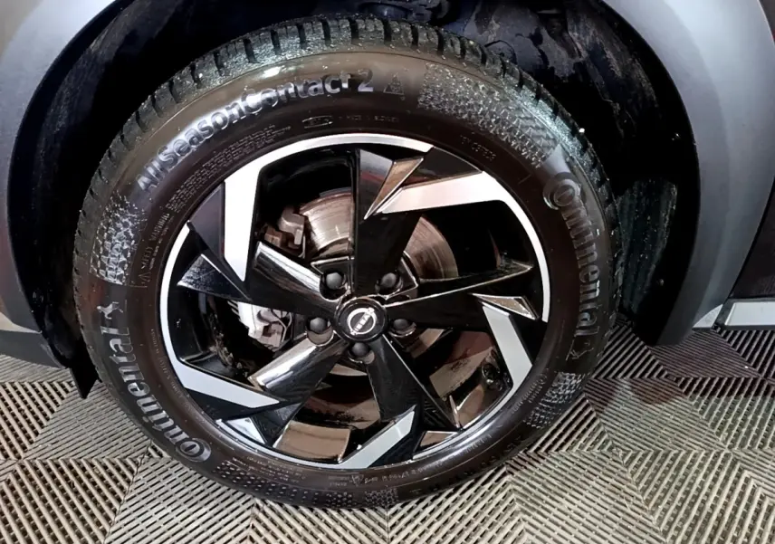 Gros plan sur la roue avant droite noire du Nissan Juke Hybrid 143 Business+ avec jante en alliage bicolore.