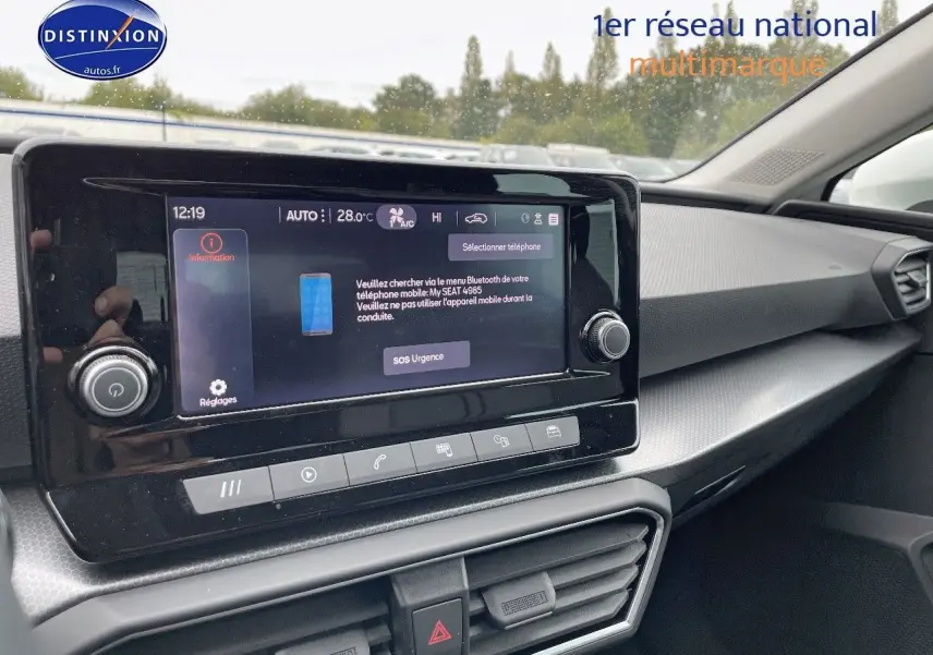 Tableau de bord et écran tactile central du SEAT LEON IV blanc, vue intérieure côté passager avec détails modernes et climatisation.