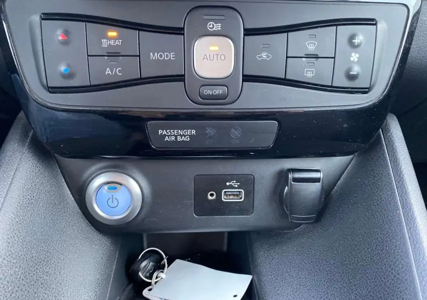 Détail de la console centrale noire de la Nissan Leaf blanche 2020, montrant les commandes de climatisation et ports USB.