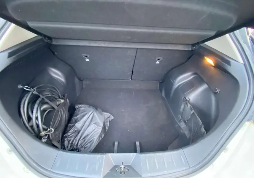 Coffre ouvert d'une Nissan Leaf blanche 2020, vue de dessus montrant un câble de recharge et un sac noir.