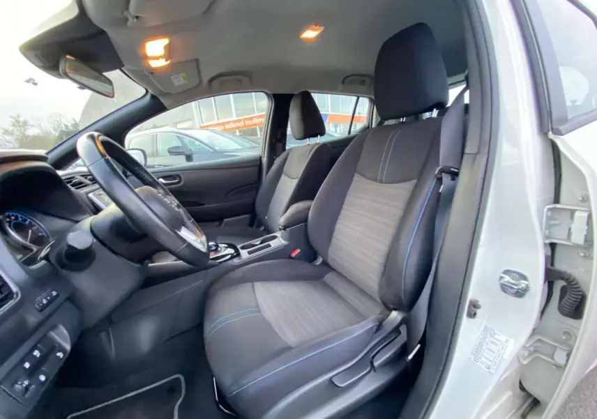 Vue intérieure côté conducteur d'une Nissan Leaf blanche 2020, sièges tissu noir et gris avec surpiqûres bleues.
