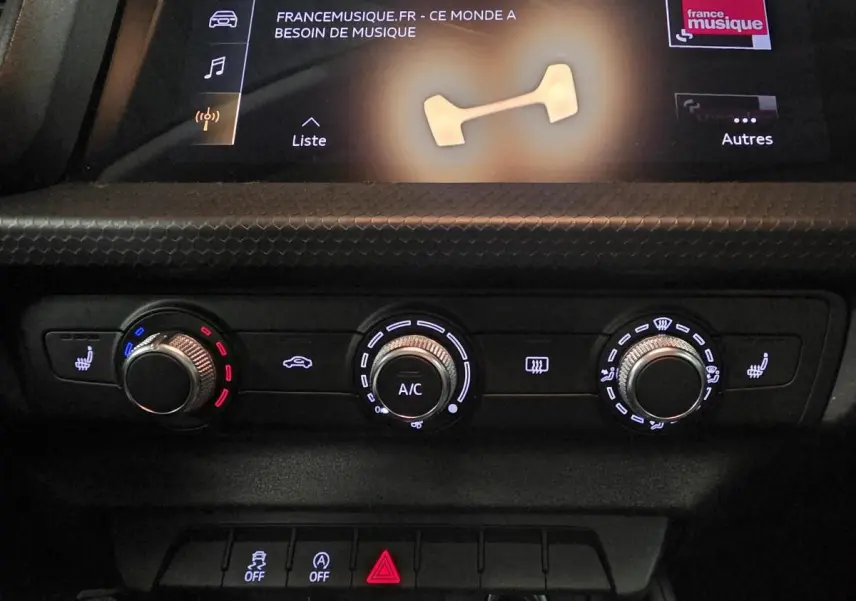 Gros plan sur la console centrale de l'Audi A1 2020, montrant les commandes de climatisation manuelle et sièges chauffants.