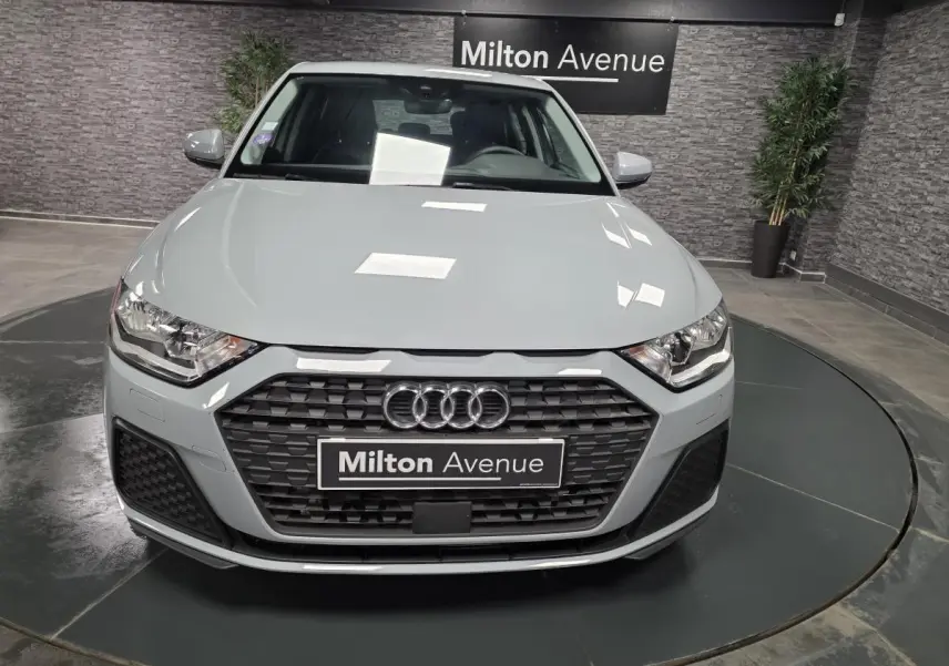 Vue frontale d'une Audi A1 Sportback gris Manhattan avec calandre noire et logo Audi visible en showroom.