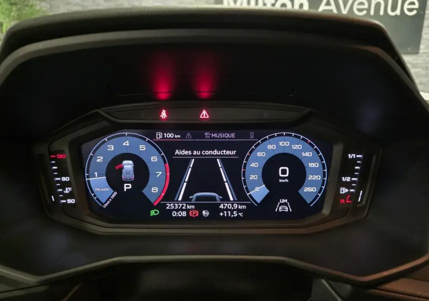 Affichage numérique du tableau de bord de l'Audi A1 Sportback gris, montrant les aides au conducteur et compteurs à 0 km/h.