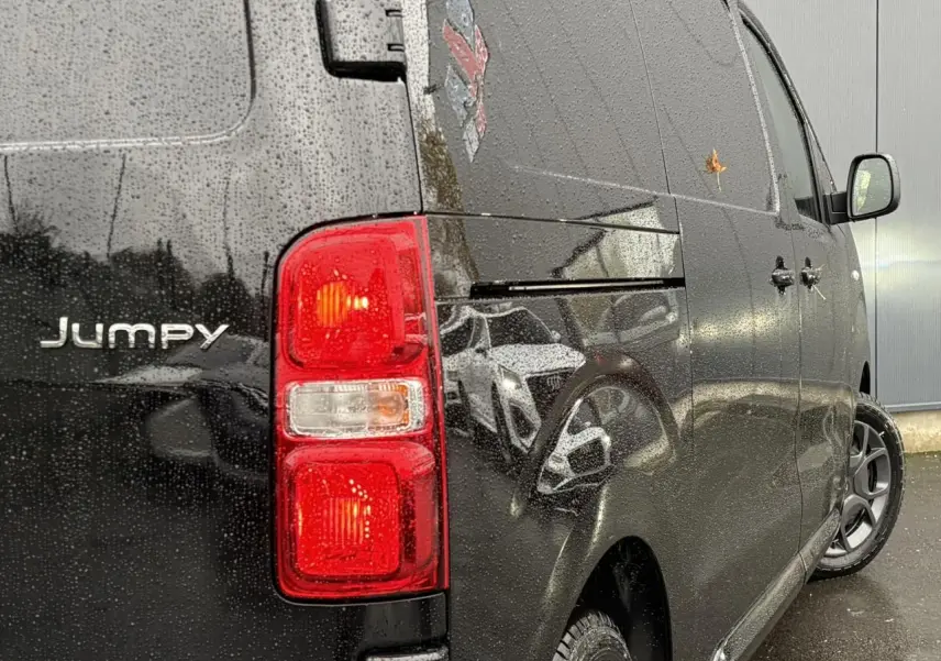 Vue arrière côté droit du Citroën Jumpy noir Perla avec feux arrière allumés sous la pluie.