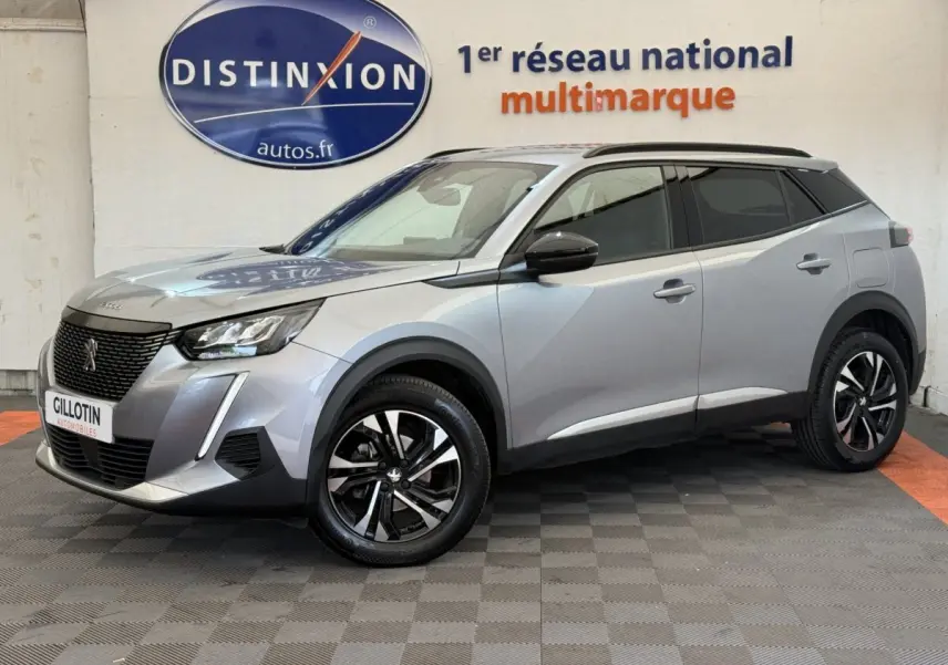 Peugeot 2008 gris clair en 3/4 avant droit, avec jantes noires et toit noir contrasté visible en intérieur showroom.