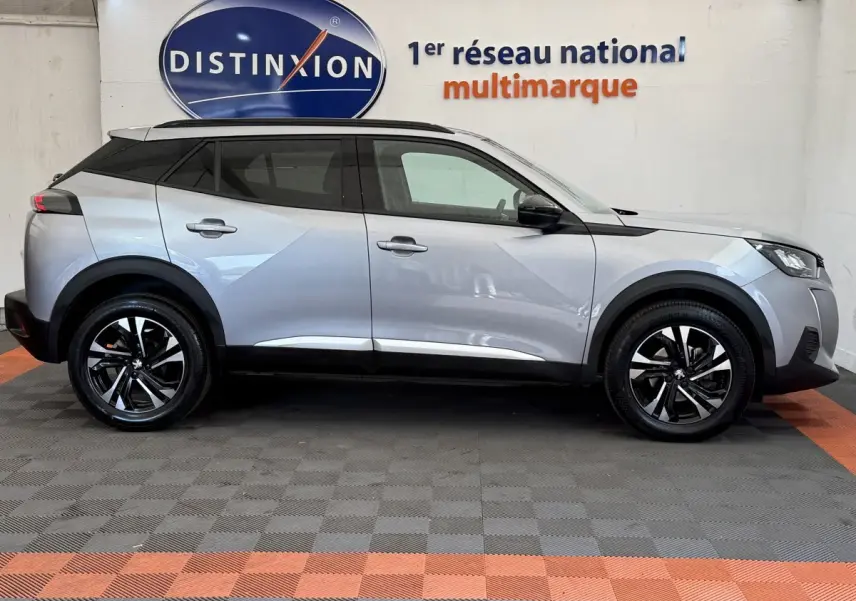 Profil droit du Peugeot 2008 gris clair 2023 avec jantes noires et toit noir contrasté, stationné en intérieur showroom.
