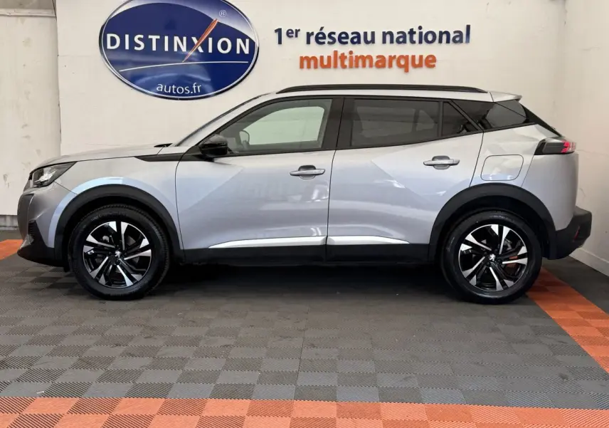 Profil côté gauche d'un Peugeot 2008 gris clair 2023, avec jantes noires et toit noir contrastant, en intérieur showroom.