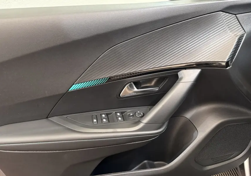 Vue rapprochée de la porte côté conducteur d’une Peugeot 2008 gris clair, avec insert décor carbone et commandes électriques.
