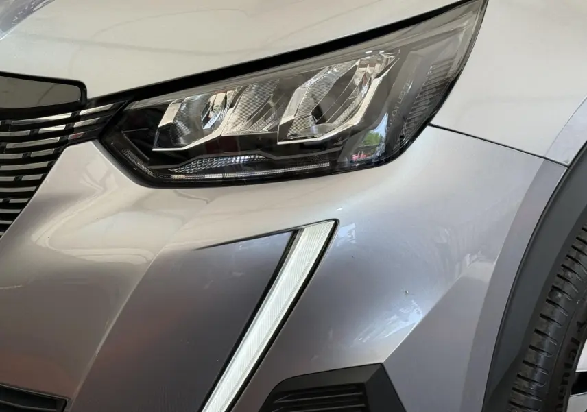 Gros plan sur le phare avant droit et la calandre d’un Peugeot 2008 gris clair avec feux LED distinctifs.