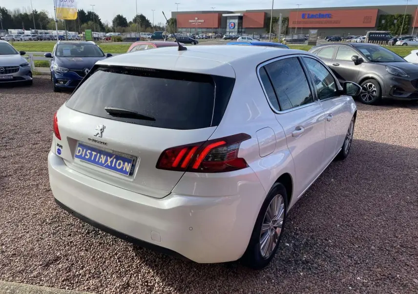 Peugeot 308 blanc nacré vue 3/4 arrière droit, vitres surteintées et feux arrière caractéristiques visibles.